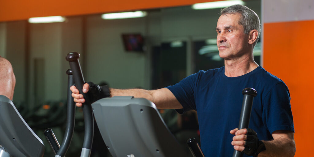 Senior man working in gym. Male adult exercising on elliptical machine. Healthy lifestyle, fitness and sports concept.