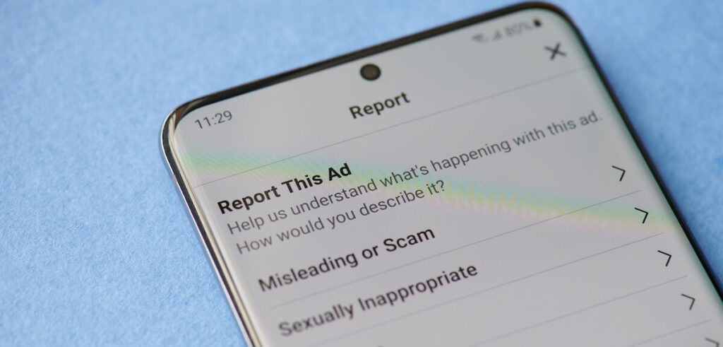 Reporting scam ads in facebook on smartphone screen close up
