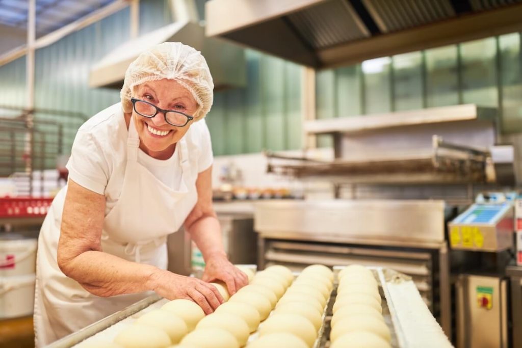 Happy senior woman as a baker with experience baking rolls in the large bakery