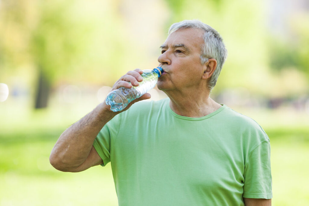 Senior man is drinking water after workout in park