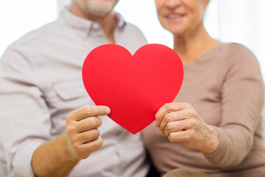 Heart health-close up of happy senior couple holding big red paper heart shape cutout at home