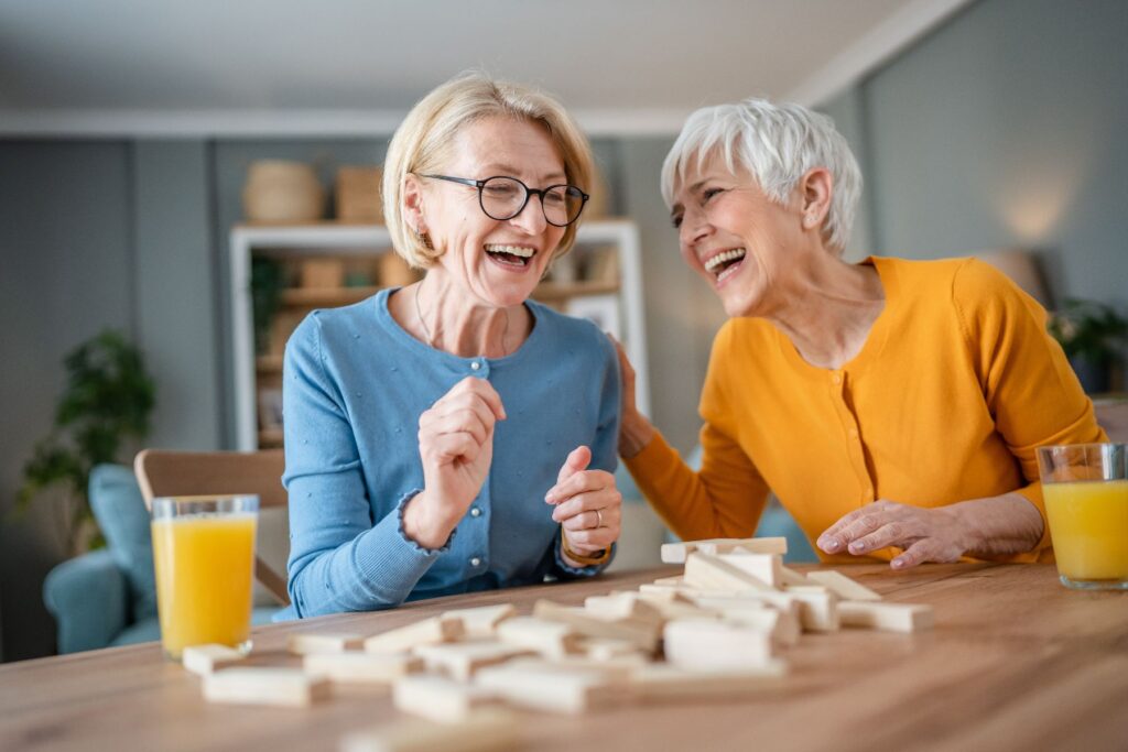 Two older adults laughing together while playing a game, representing the truth behind myths about independent living.